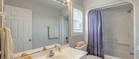 Un baño con un lavamanos blanco, un espejo con iluminación, un inodoro y una ducha con cortina morada.