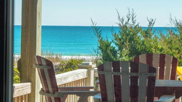 Una terraza de madera con sillas Adirondack con vista a una playa y al océano.