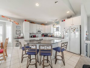 A modern kitchen with white cabinets, a granite island, and bar stools. - Serendipity by Topsail Realty (Holly Ridge)