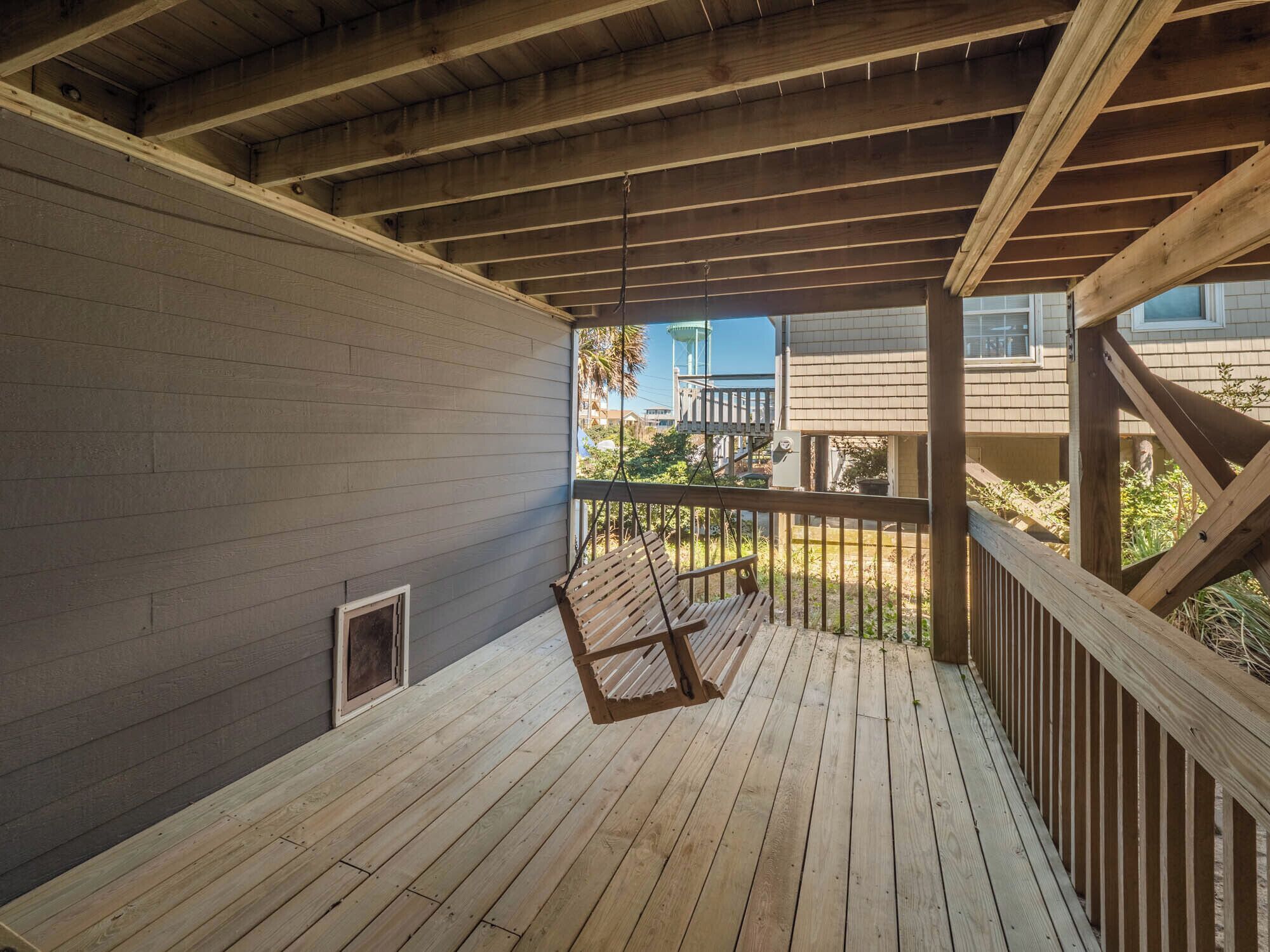 A covered wooden deck with a bench, a metal railing, and a view of a building with a water tower in the background.