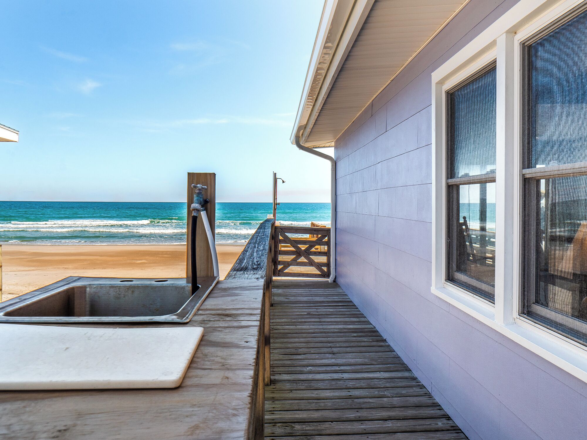Een houten terras dat naar een strand leidt, met uitzicht op de oceaan.