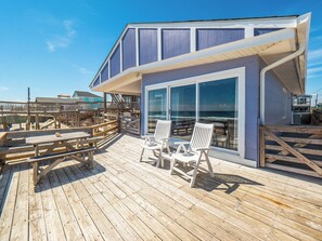 A wooden deck with outdoor seating and a large glass window overlooking the ocean. - Mamaw's Spot by Topsail Realty (Holly Ridge)