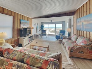 Relax in this spacious living room with a large TV, comfortable sofa, and dining table, offering a view of the beach.