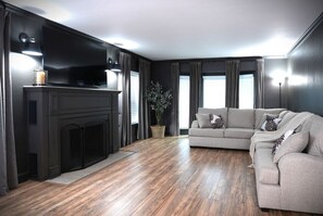 A modern living room with a fireplace, a sofa, and a television. - Designer decorated 6 bedroom 4 bath pool home (Santa Ana)