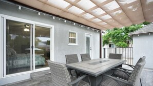 Eine überdachte Terrasse mit Esstisch und Stühlen, einer Schiebetür aus Glas und einem kleinen Fenster.
