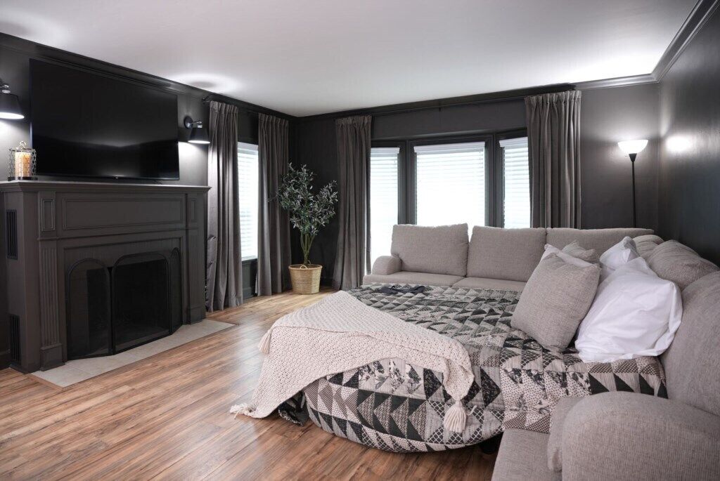 A modern living room with a fireplace, a large flat-screen TV, a sofa, and a patterned ottoman.