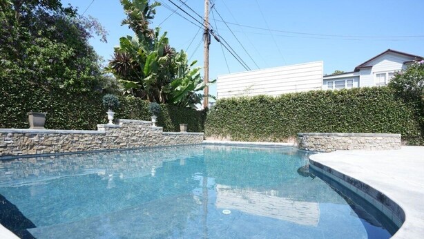 Ein Pool mit einer Steinmauer und einer Hecke im Hintergrund.