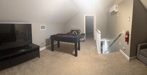 A room with a foosball table, a television, and a staircase leading to another area.