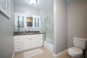 A bathroom with a glass-enclosed shower, a white toilet, and a vanity with drawers and a mirror.