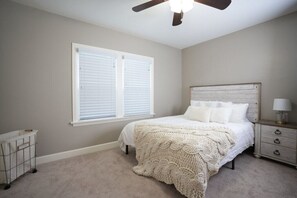 A bedroom with a bed, a nightstand, a lamp, a ceiling fan, and a window with blinds.