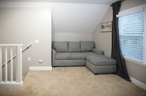 A corner room with a gray sectional sofa, a white railing, and a window with blinds. - Designer decorated 6 bedroom 4 bath pool home (Santa Ana)