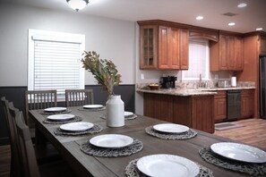 A dining area with a long wooden table set with plates and a vase of greenery.