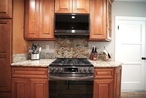A kitchen with wooden cabinets, a granite countertop, a stainless steel stove, and an oven. - Designer decorated 6 bedroom 4 bath pool home (Santa Ana)