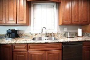 A kitchen with wooden cabinets, a granite countertop, a stainless steel sink, a coffee maker, a toaster, and a dishwasher. - Designer decorated 6 bedroom 4 bath pool home (Santa Ana)