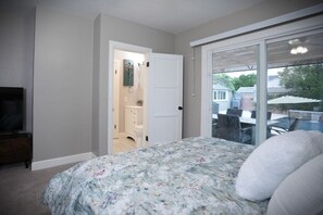 A bedroom with a bed, a TV, a bathroom, and a sliding glass door to an outdoor area. - Designer decorated 6 bedroom 4 bath pool home (Santa Ana)