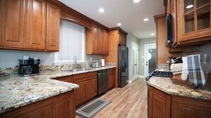 Una cocina con gabinetes de madera, encimeras de granito, un refrigerador de acero inoxidable y una cafetera.