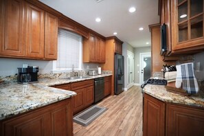 Una cocina con gabinetes de madera, encimeras de granito, un refrigerador de acero inoxidable y una cafetera.