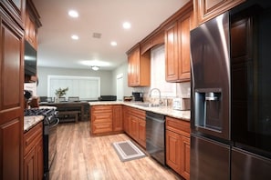 A kitchen with wooden cabinets, stainless steel appliances, and a granite countertop. - Designer decorated 6 bedroom 4 bath pool home (Santa Ana)