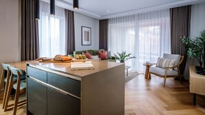 Ett modernt vardagsrum med en central köksö, en soffa, en fåtölj och en matplats med stolar och ett bord.