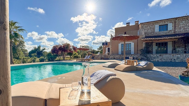 A poolside area with lounge chairs, a wooden table with a glass, and a stone building in the background.