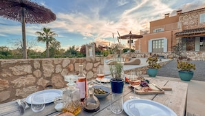 A table set for a meal with a bottle of wine, glasses, and a loaf of bread on a wooden table outdoors.