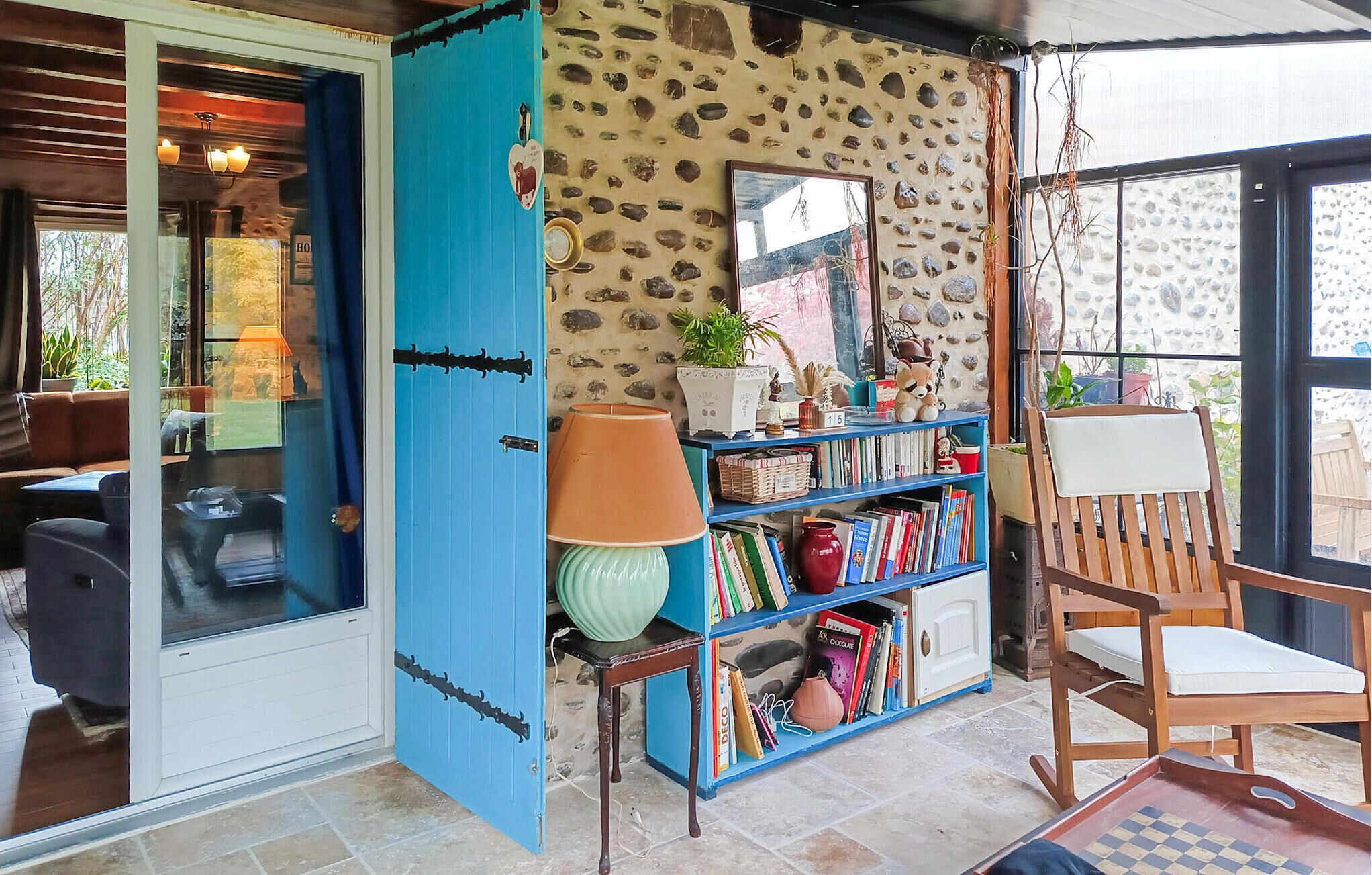 A cozy room with a blue door, a bookshelf, a wooden chair, and a window with a view.