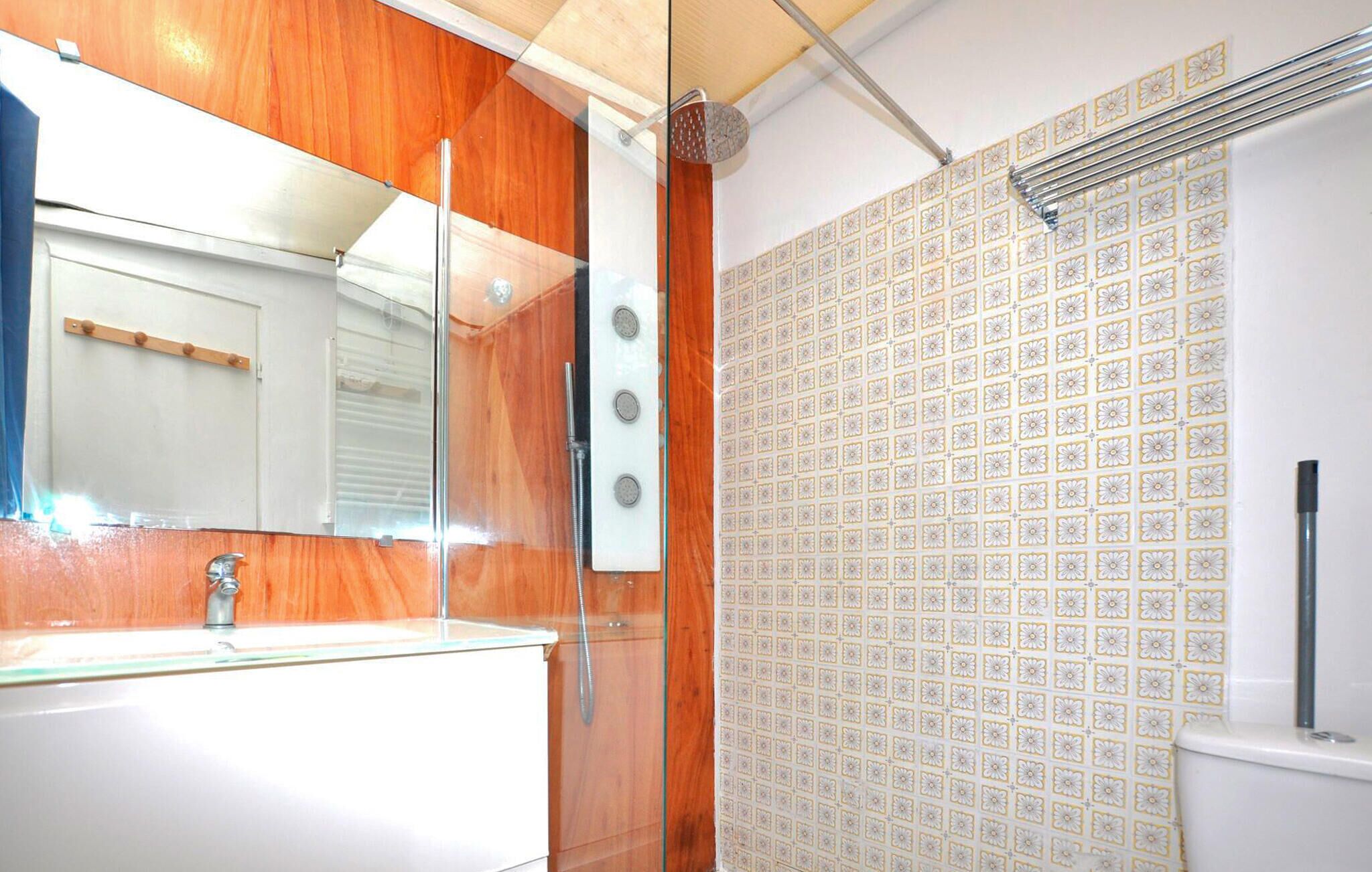 A bathroom with a wooden vanity, a mirror, a shower with a tiled wall, and a toilet.