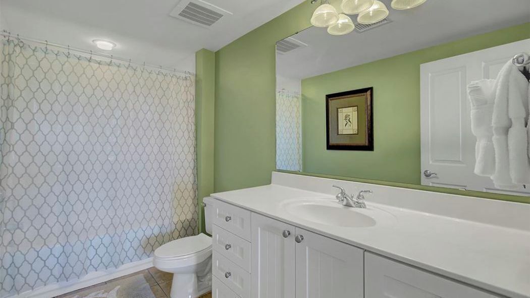 Un bagno con un lavandino bianco, un quadro appeso al muro e un asciugamano bianco appeso alla porta.