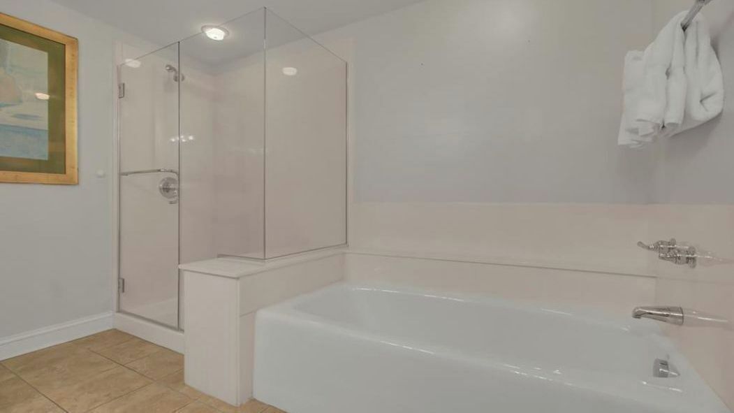 A bathroom with a glass-enclosed shower, a white bathtub, and a towel rack.