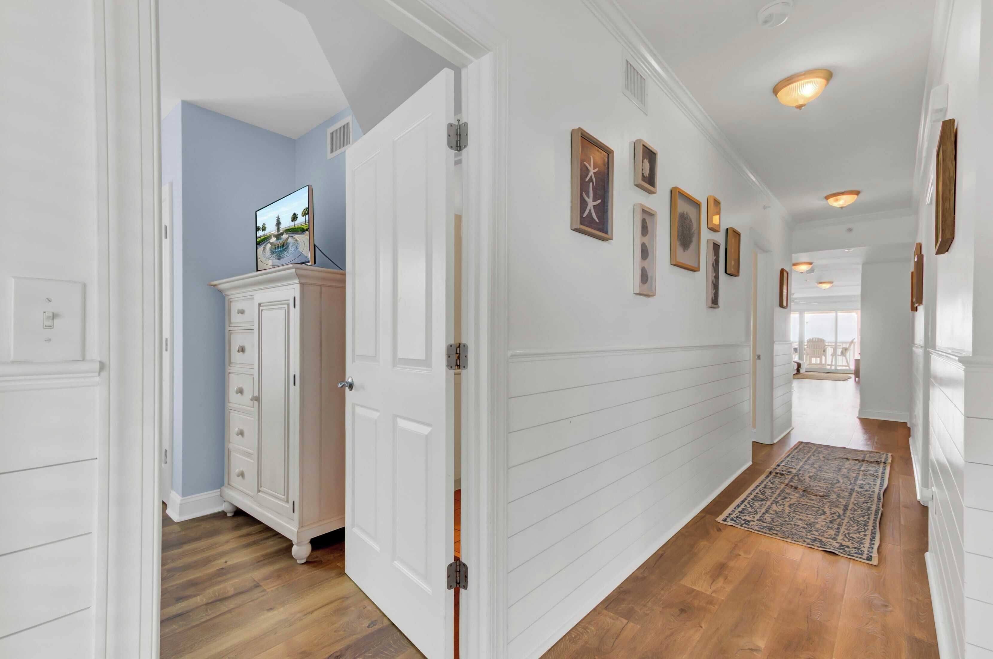 A hallway with white paneling, a wooden floor, and a rug.