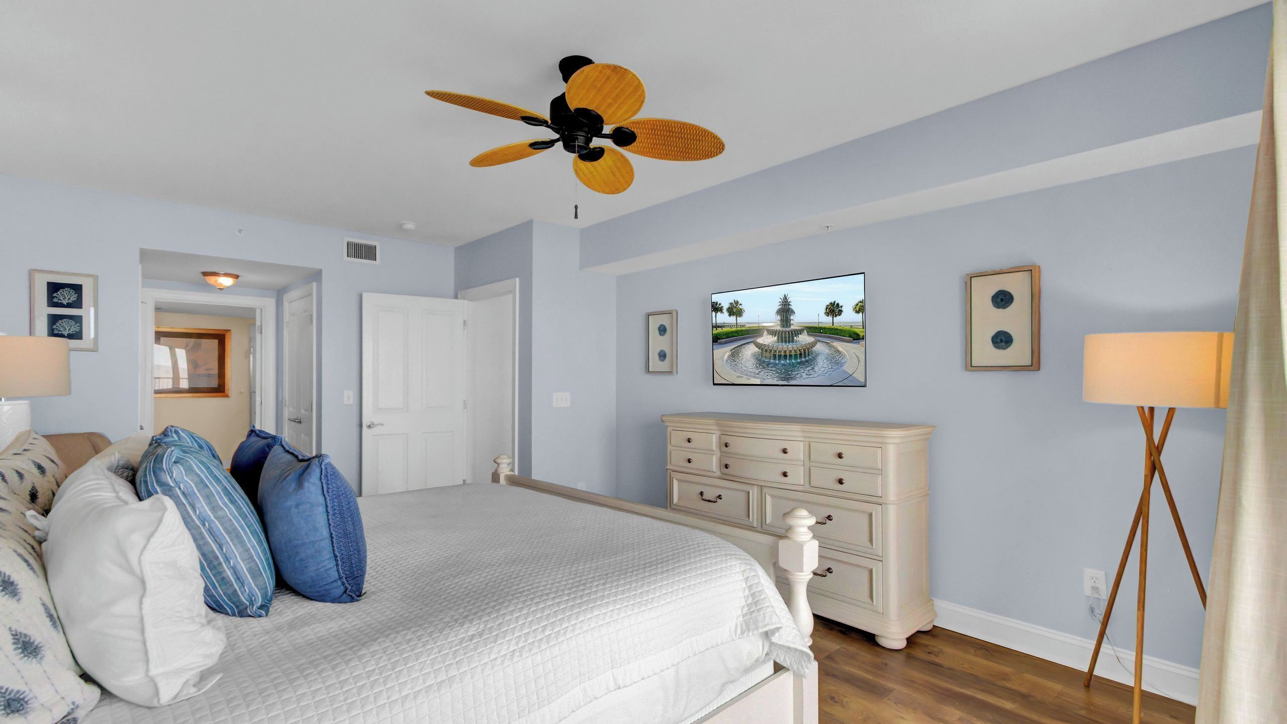 A bedroom with a bed, a dresser, a ceiling fan, a TV, and a lamp.