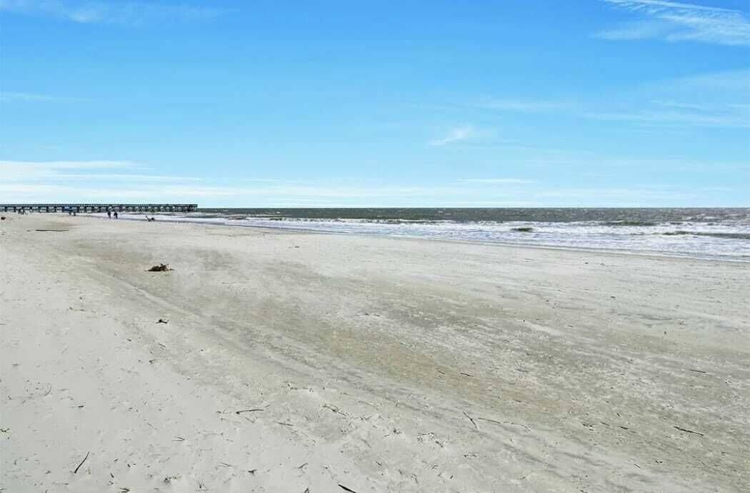 A beach with a pier extending into the water, sandy shore, and clear skies.