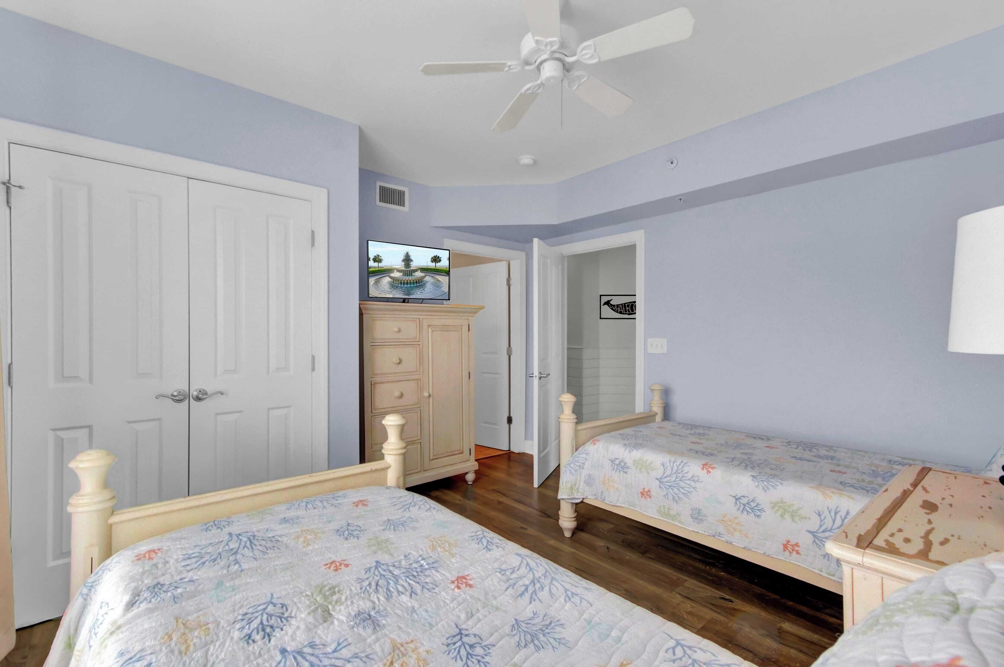 A bedroom with two single beds, a ceiling fan, a TV on a dresser, and a wardrobe.
