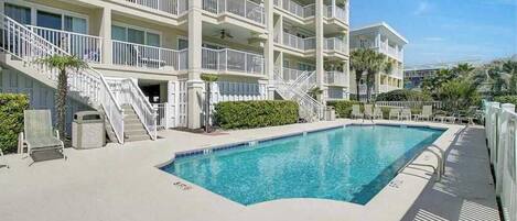 A multi-story hotel with a swimming pool, outdoor seating, and a clear blue sky.