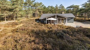 Moderni mökki, jossa on suuri terassi, ja se on ympäröity tiheällä metsällä.