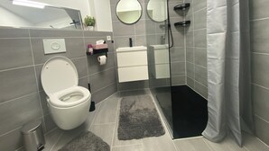 Un baño moderno con inodoro, lavamanos, dos espejos, ducha y un pequeño cubo de basura.