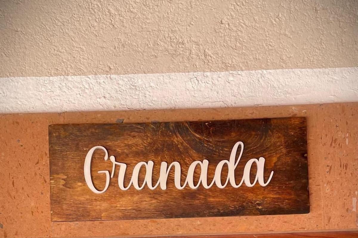 A wooden sign with the word "Granada" on a textured wall.