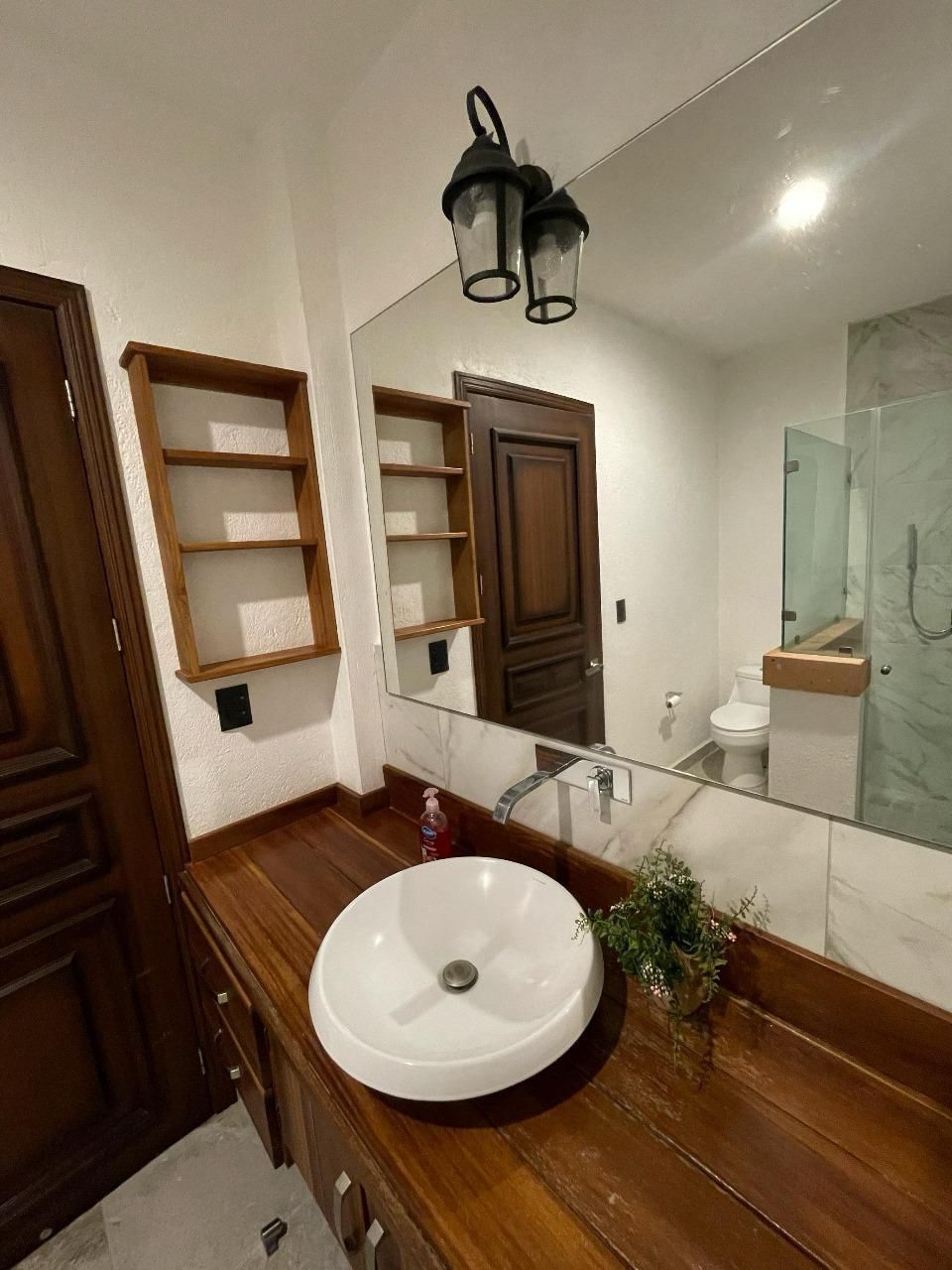 A bathroom with a wooden vanity, a white sink, a large mirror, and a glass shower enclosure.