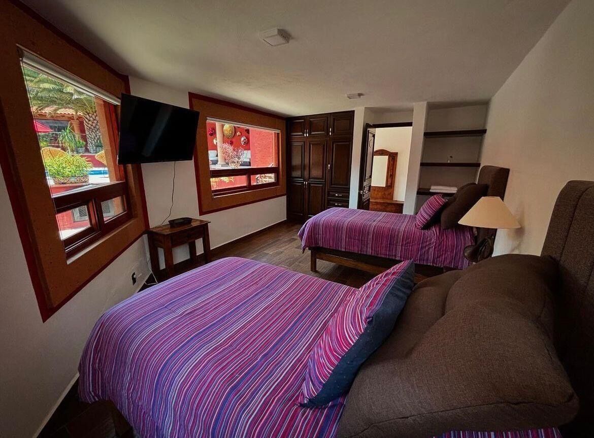 A bedroom with two beds, a TV, and a window with a view of a garden.