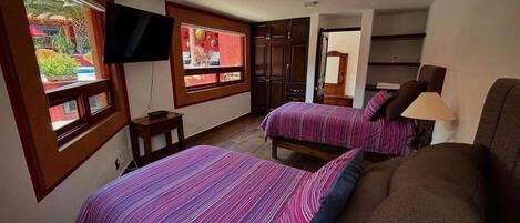 A bedroom with two beds, a TV, and a window with a view of a garden.