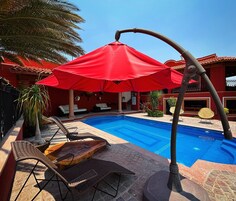 Una piscina con sombrilla roja, mobiliario de mimbre y zona de patio con baldosas.