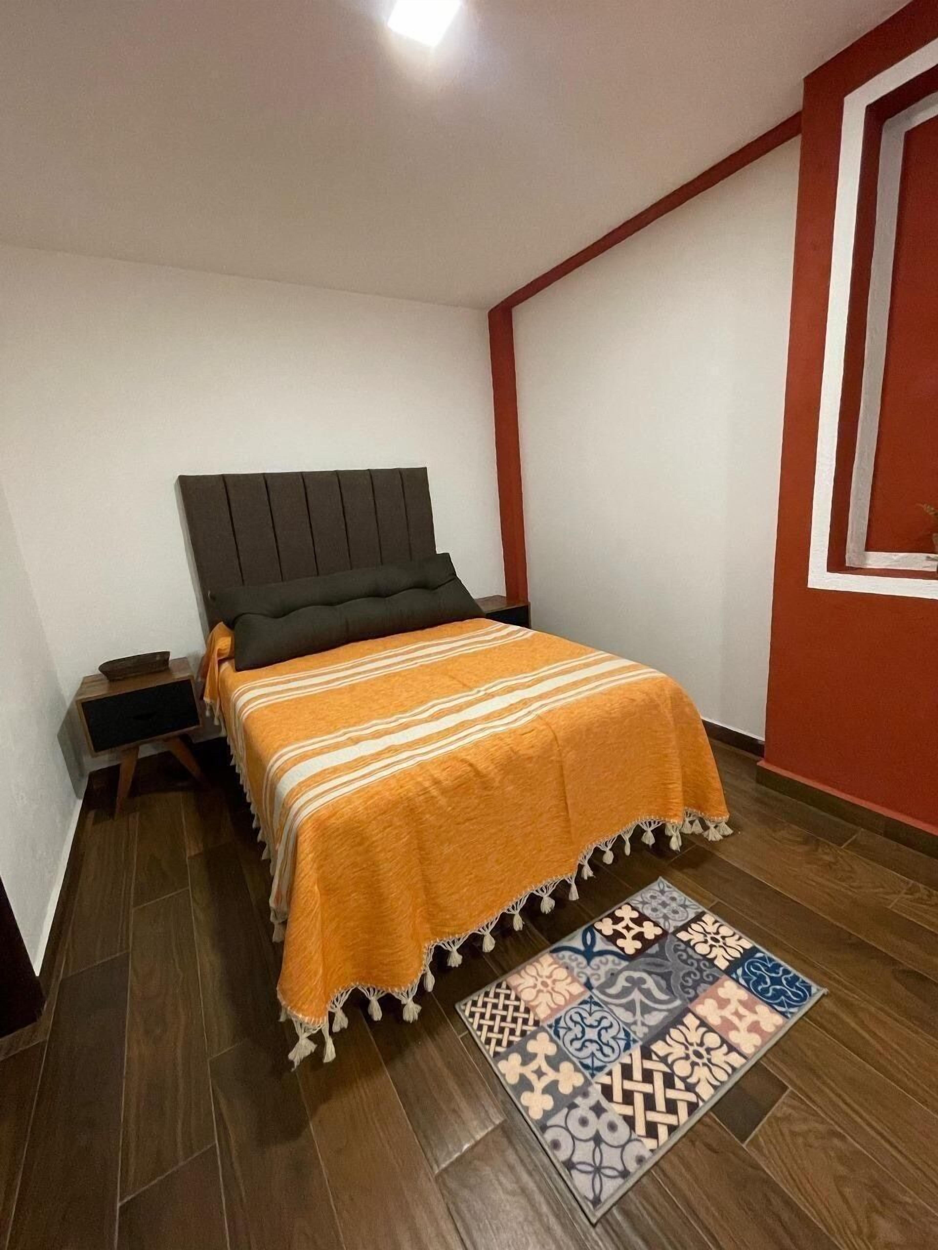 A bedroom with a bed, nightstand, and a patterned rug.