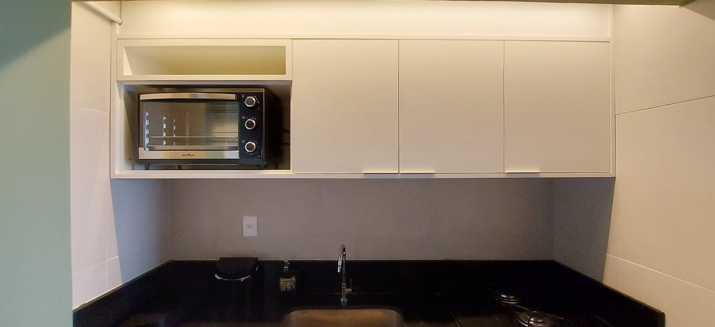 Een kleine kitchenette met een ingebouwde magnetron, een spoelbak en een aanrecht.