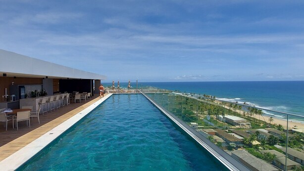 Un espace aménagé au bord de la piscine, avec vue sur l’océan, des sièges extérieurs et un bar.