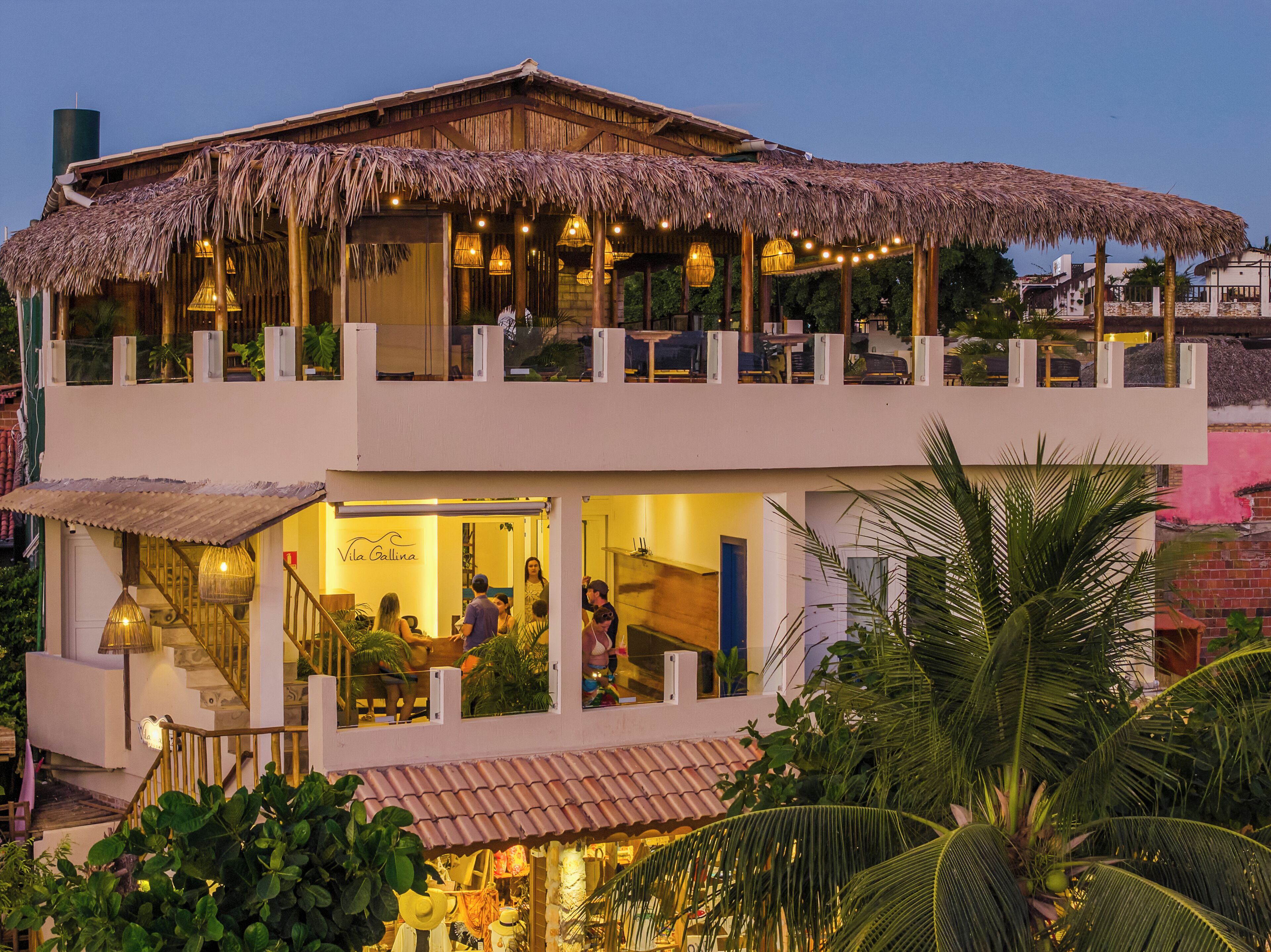 A two-story building with a thatched roof, a visible restaurant on the ground floor, and a balcony with seating.
