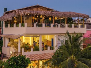 Un edificio de dos pisos con techo de paja, un restaurante visible en la planta baja y un balcón con asientos.