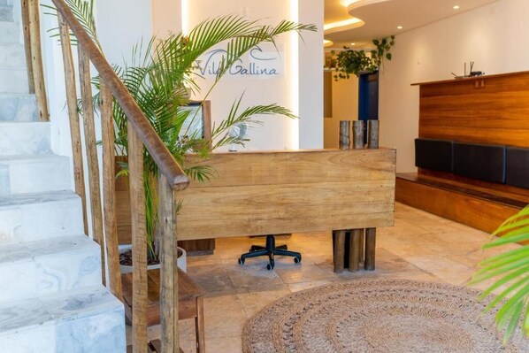A modern lobby with a wooden reception desk, a staircase, and a large plant. - VILA GALLINA POUSADA (Jijoca de Jericoacoara)