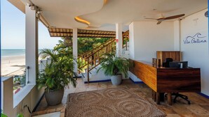 A hotel room with a view of the beach, a wooden desk, a ceiling fan, and a staircase leading to an upper level.