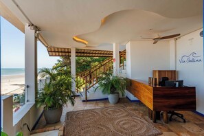 Ein Hotelzimmer mit Blick auf den Strand, einem Holztisch, einem Deckenventilator und einer Treppe, die zu einer oberen Ebene führt.