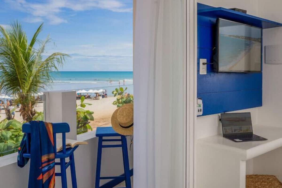Un balcon donnant sur la plage, un ordinateur portable et un chapeau de paille posés sur une table.